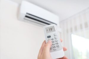un telecomando di un condizionatore in primo piano e sullo sfondo un condizionatore