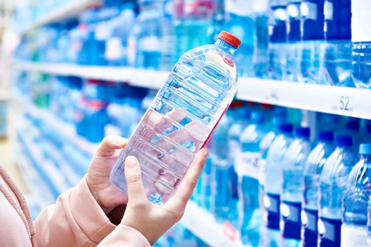 persona che prende una bottiglia di acqua da uno scaffale del supermercato