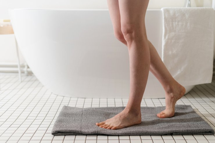 persona appena uscita dalla doccia che mette i piedi su un tappetino