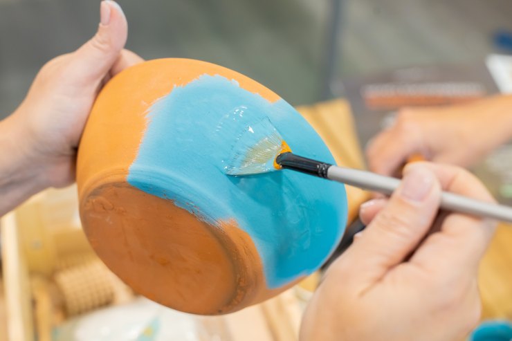 persona che colora una stoviglia in ceramica con un pennello 