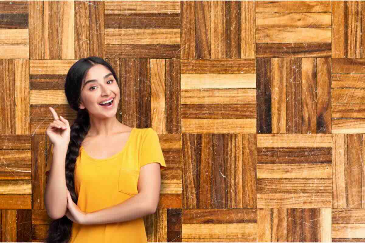 Ragazza sorridente con dito alzato, sul fondo parquet graffiato
