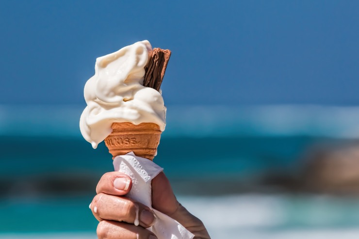 Un cono gelato in mano ad una persona con sfondo il mare