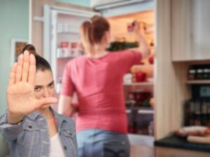 donna che ripone alimenti in frigorifero e un'altra che fa stop con le mani