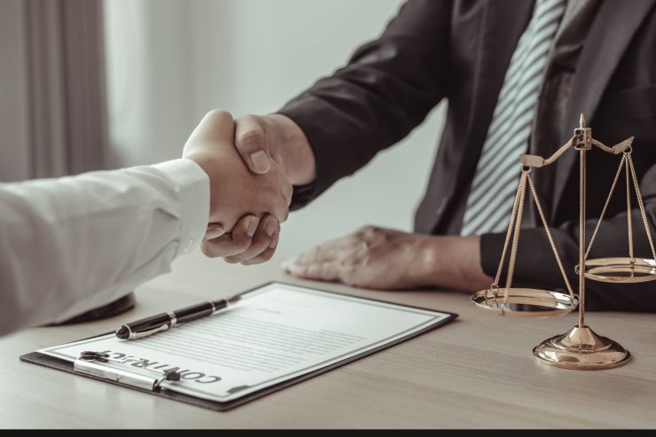 persone che si stringono la mano quasi come se avessero accordato delle regole, c'è una scrivania sulla quale ci sono dei fogli una penna ed una bilancia che è il simbolo della giustizia