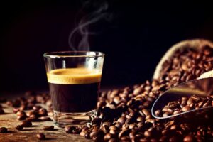del caffè in un bicchierino che fuma, con dei chicchi di caffè tutto attorno