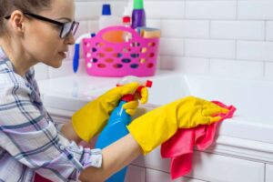 Donna intenta a pulire la vasca con prodotto spray e panno