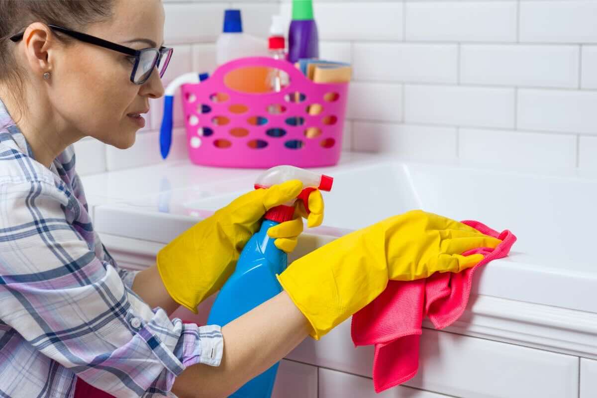 Donna intenta a pulire la vasca con prodotto spray e panno
