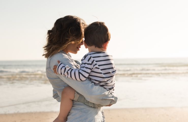 la mamma che tiene in braccio il figlio in riva al mare