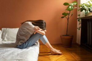 Donna con capo sulle gambe, seduta a letto, triste