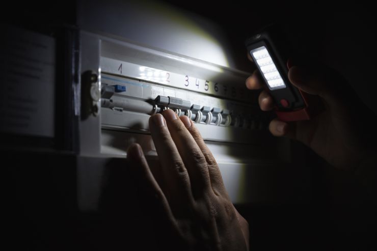 persona con una torcia che controlla il quadro elettrico