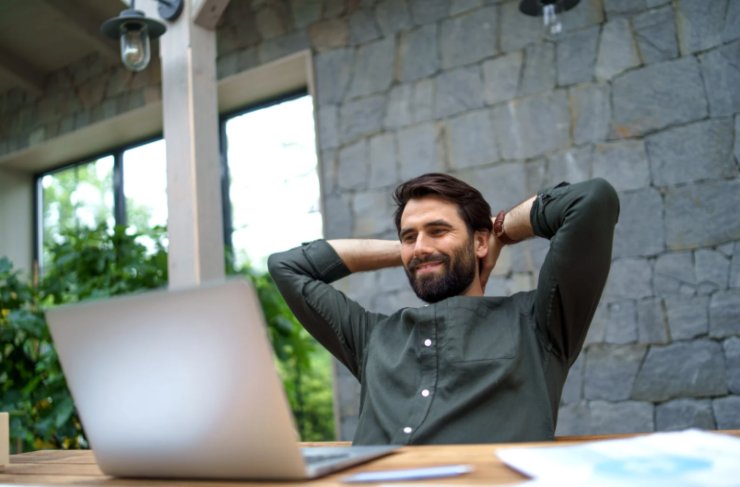 uomo che sorride con le mani dietro alla testa seduto davanti al computer