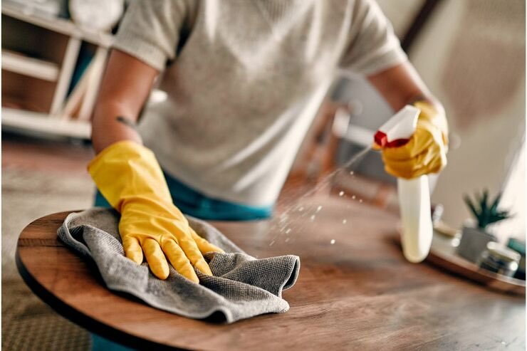 Mano spruzza su tavolo di legno un prodotto, con altra mano con guanto usa un panno in microfibra