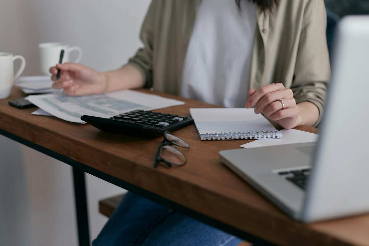 Donna che fa i calcoli alla scrivania con pc e calcolatrice