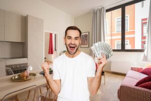 un salone di una casa con un uomo in primo piano che esulta con dei soldi in mano