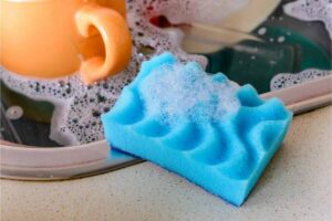 Spugna per i piatti con schiuma vicino lavandino con tazza