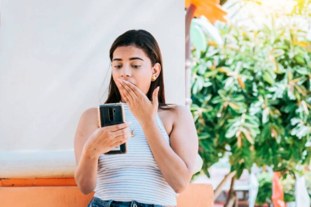 donna stupita con il cellulare in mano e l'altra mano sulla bocca